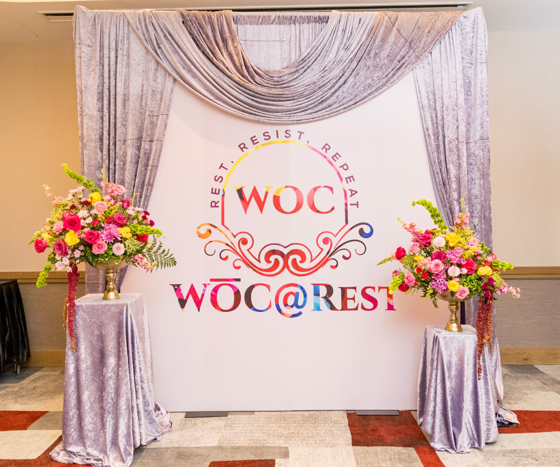 WŌC @ Rest® event backdrop framed by colorful flower arrangements